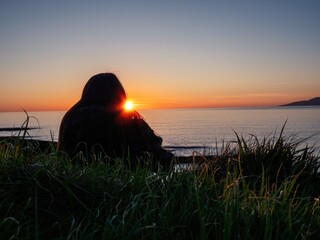 Silhouette of a girl watching sunset over ocean. Dark and moody nature. Outdoor activity....