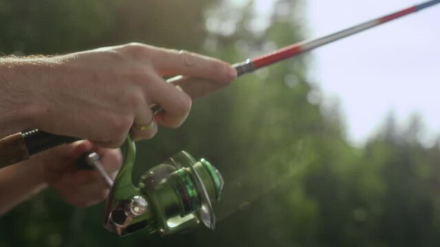 Closeup of unrecognizable hands of fisherman spinning reel on his rod while fishing outdoors in nature