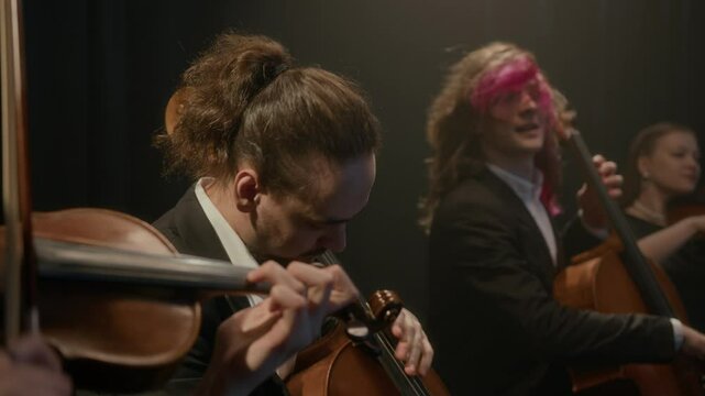 Medium shot of talented Caucasian string quartet starting their music performance of stage, playing violins and cellos live on black background
