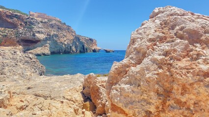 Turquoise sea water and Limestone cliffs with small natural arch in the background. Comino island view from the Moon beach. High quality photo