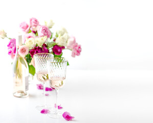 A bottle and two glasses of rose wine and a bouquet of pink roses