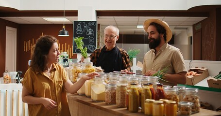 Elderly vendor assisting clients in eco friendly shop with ethical sourced food items, providing recommendations. Woman and man in local store chatting with trader about bulk products