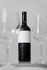 Bottle and glass of red wine with a composition several wine glass and holding hand. Minimalistic composition on a white background for product branding, identity, and packaging.