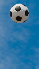 vertical image of soccer ball in the air by kick on day with blue sky and clouds, sports and fun theme