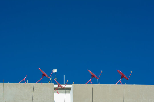 antena parabolica de se&ntilde;al satelital de color rojo sobre techo en fondo de cielo azul