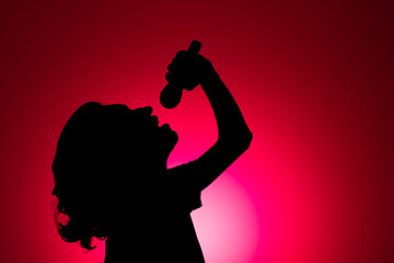 Silhouette of young man holding wireless microphone singing music with head up.
