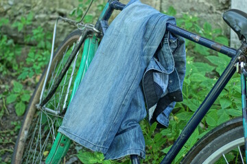 one blue cotton jeans hanging on the frame of a bicycle in the green grass on the street