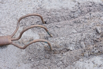 one small brown iron rake lies on the gray sand outside