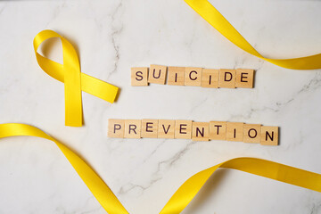 Yellow ribbon, symbol of the world suicide prevention day, on white marble background.