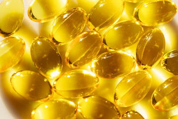 Bowl filled with yellow fish oil, rich in omega-3 fatty acids. Pills are oval shaped and are yellow in color. They are arranged in a pile on a white surface