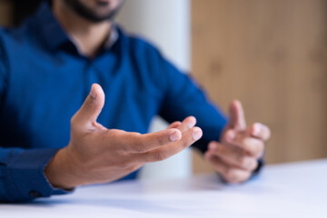 Gesturing with hands, man in blue shirt discussing business at office table, copy space