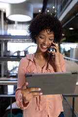 Smiling woman using tablet and talking on smartphone in modern office