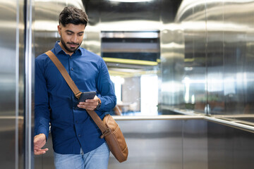 Using smartphone, man with messenger bag standing in elevator, checking messages, copy space