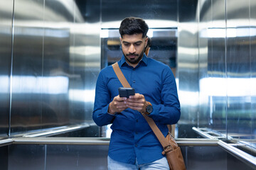 Using smartphone, man in blue shirt checking messages in elevator © wavebreak3