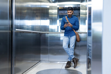 Using smartphone, man standing in elevator, wearing casual business attire, copy space © WavebreakMediaMicro