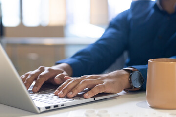 Typing on laptop, man working in office with coffee mug on desk