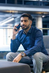 Talking on smartphone, man sitting in office, wearing blue shirt and jeans