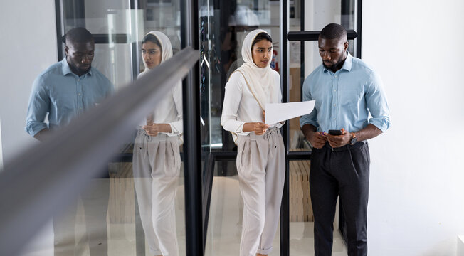 Business colleagues walking in office, reviewing documents and using smartphone