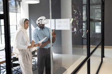 Using VR headset, business professionals brainstorming and writing on glass board in office, copy sp