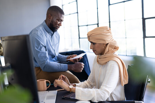 Working in office, woman using computer while man holding documents nearby