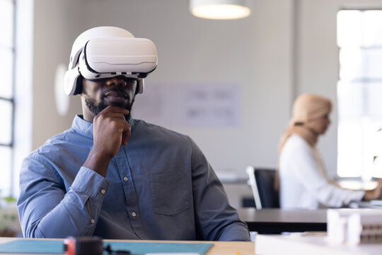 Using VR headset, businessman sitting at desk in modern office environment