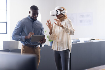 Using VR headset, woman interacting while man holding tablet in modern office