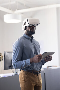 Using VR headset, businessman holding tablet and exploring virtual reality in office