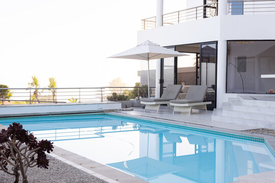 Luxury vacation, poolside lounge chairs and umbrella by modern villa, copy space