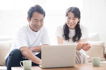 明るい綺麗なリビングでパソコンを見ながら話し合う50代夫婦