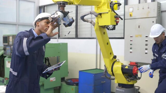 African American technician work with his team to check and maintenance robotic arm in factory workplace.