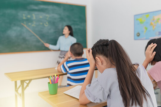 close up asian girl, asian student group studying mathematics with female teacher, asian girl use hand touch on her head, they feeling bore and unhappy in classroom, problem in elementary school