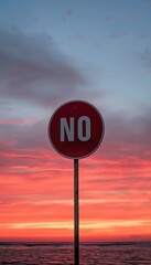 A red no-entry sign stands tall against a stunning sunset with vibrant colors of orange, pink, and blue sky over the calm water.