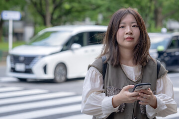 Young Chinese woman in her 20s standing on a public road near Shiba Park in Minato Ward, Tokyo, holding a smartphone