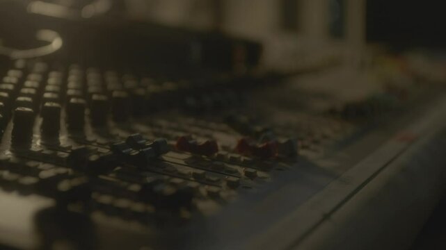 Technician moves levers up on equalizer console in semi-dark studio closeup. Producer processes tracks on control panel. Making music