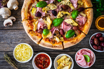 Circle pizza capricciosa slices prepared with cooked ham, mozzarella, artichoke, sliced mushrooms and olives on wooden table
