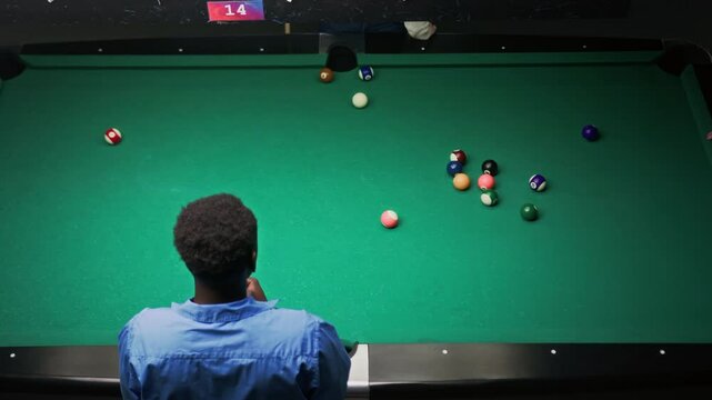 High angle slowmo shot of African American man playing billiards on green table in bar