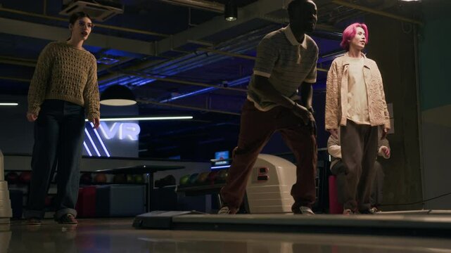 Full shot of four multiethnic gen z friends spending good time playing bowling game together in bowling alley
