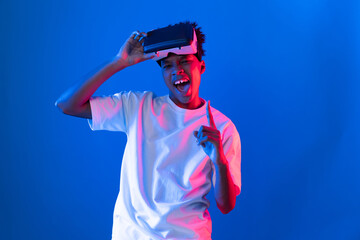 Young African American gaming player wearing VR pointing hologram 3D graphic isolated blue pink...