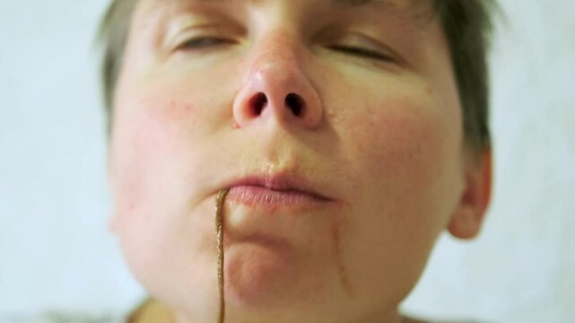 Close-up of the face of a young woman eating Chinese noodles using chopsticks while chewing her lunch in slow motion.