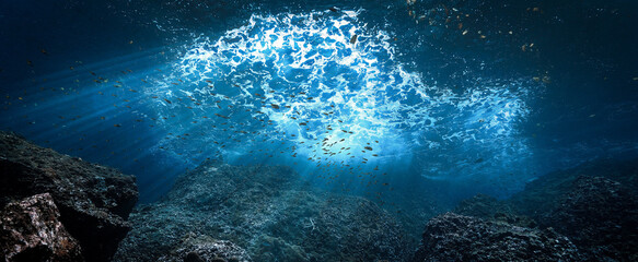 Underwater photo of rays of sunlight in blue colors coming through the surface over a reef. 