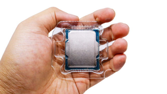 A man's hand holds a new computer processor in its original packaging tray. A close-up shot of a CPU processor in its plastic packaging against a white background.