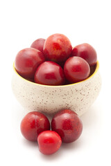 Front view of fresh Cherry Plum (Prunus cerasifera) fruits spilled out from a ceramic bowl on a white background.