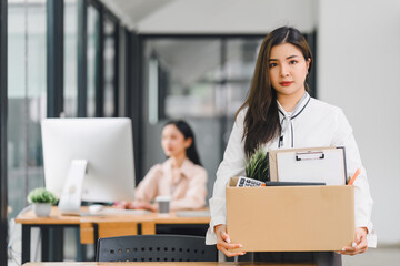 Employee packing personal belongings into cardboard box after receiving layoff notice in modern office.