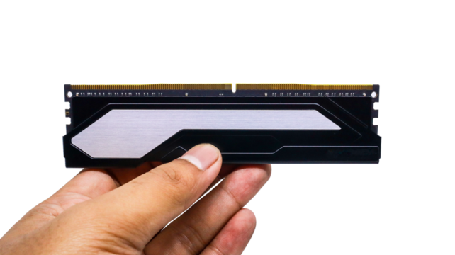 A close-up of a black and white RAM stick held in a hand against a white background. RAM modules feature black heatsinks with gold connectors isolated on a white background.