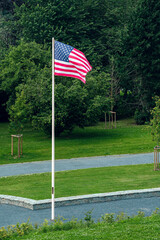 American flag on pole waving in the wind in front of trees at Mardasson Mermorial in Bastogne, Belguim