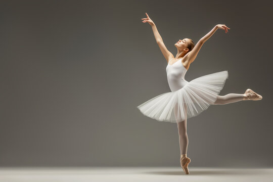 A ballerina in a white tutu performs an elegant pose on stage, capturing the timeless beauty and grace of ballet with perfect balance and poise in a minimalistic setting.