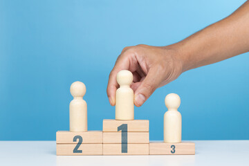 Concept of success, winner and victory in business. A man holding wood person model standing on award podium. Leadership and superiority