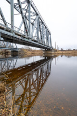 A metal truss bridge over the river in overcast spring day. Natural springtime scenery in Riga, Latvia.
