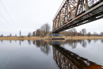 A metal truss bridge over the river in overcast spring day. Natural springtime scenery in Riga, Latvia.