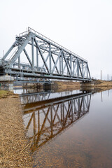 A metal truss bridge over the river in overcast spring day. Natural springtime scenery in Riga, Latvia.